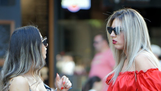 two women wearing sunglasses standing in front of each other talking